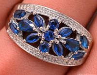 Front angled view of silver ring showing blue sapphire cluster and clear accent stones