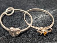 Close-up of both silver-tone rings showing heart charm and bow knot designs