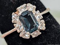 Close-up of ring top showing blue emerald-cut stone and clear halo stones