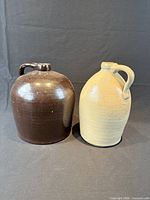 Front view of two stoneware jugs, brown and cream, showing shape, handles and glaze