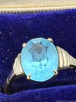 Close-up of ring showing oval light blue gemstone and gold setting