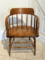 Front view of wooden captain’s chair showing spindle back, curved arms, turned legs