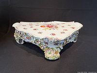 Overall view of porcelain display stand showing rococo floral decorations and scroll feet