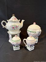 Front view of both teapots, sugar bowl and creamer showing designs and pedestal warmers