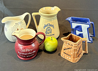 Group shot showing all five ceramic advertising whisky jugs with apple for scale