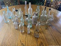 Group shot of approximately twenty-eight clear and aqua glass bottles on wooden table, assorted shapes and sizes