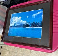 Front view of framed tropical island print in brown wood frame with black mat