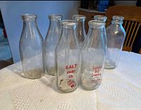 Group of seven clear glass milk bottles on table