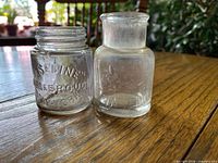 Front view of both clear glass Vaseline jars showing embossed lettering.