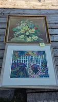Two framed artworks laid on wood surface: floral painting on top, garden print below