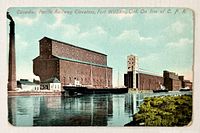 Front view of colour postcard showing grain elevators and waterway