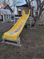 Side view of entire yellow fiberglass slide mounted on wooden structure