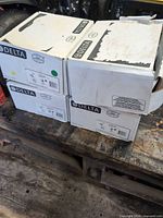 Four Delta boxed shower trim kits stacked on workbench