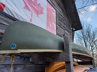Side view of green fiberglass canoe stored upside down on rack