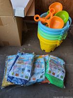 stack of five multicolour castle buckets with scoops resting on top, four packaged mesh bags in foreground