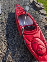 Full top view of red Pelican kayak on gravel with paddle across cockpit