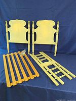 all disassembled components of the doll bed including headboard, footboard, side rails, slat base, and hardware bag displayed on blue backdrop