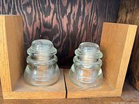 Pair of wooden L-shaped bookends each holding a clear glass insulator