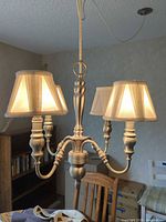 Full view of four-arm brushed brass chandelier with shades lit