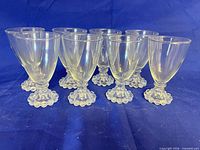 Eight clear glass hobnail goblets arranged on blue backdrop