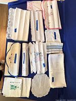 All 15 assorted white linens laid out on blue surface showing embroidery, lace and overall condition