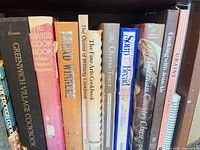 Shelf one showing hardcover cookbooks including Greenwich Village Cookbook, The Swiss Cookbook, Bread Winners, Fine Arts Cookbook, Soup & Bread, The Olive’s Table, American Country Cheese, Grains