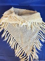 cream knit triangular shawl with fringe on blue background