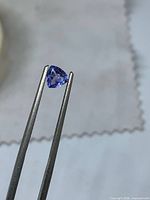 Front view of triangular tanzanite held by tweezers