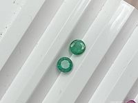 Two round green emeralds on white background showing color and cut