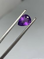 Front view of pear-shaped purple amethyst held in tweezers