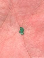 Two oval green emeralds in palm for size reference