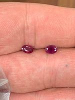 Two small faceted red oval gemstones on fingertip
