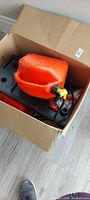 Fuel caddy inside box showing orange tank, pump components and base