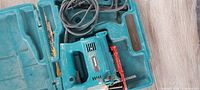 Open teal Makita case holding corded jig saw, blades and power cord visible
