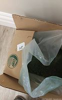 Open cardboard box with plastic liner holding green sweeping compound