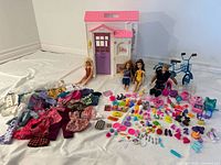 Overview showing Barbie house, three dolls, blue bicycle, clothing pile, and spread of accessories