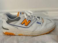 Side view of left shoe New Balance 550 white leather with orange N and blue trim