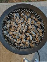 Top view of black metal fire pit filled with lava rocks, showing lattice sides and attached propane hose