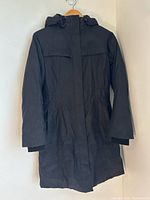Front view of black The North Face down parka showing length, hood, storm flap