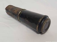 Closed telescope showing black lacquer barrel, brass trim, deteriorated leather wrap
