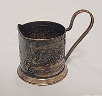 Front view of ornate silver-plated tea glass holder showing floral relief and medallion