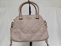 Front view of quilted leather satchel showing logo, handles, strap attachment