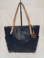 Front view of navy blue Michael Kors Jet Set tote showing MK charm, beige straps, side pockets