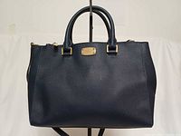 Front view of dark blue saffiano leather satchel with handles and logo plate