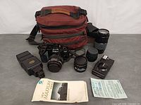 Group view showing camera bag, SLR with lens, three additional lenses, flash, compact camera, manual, paperwork