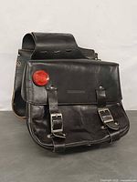 Front angled view of one saddle bag showing buckles, reflector, leather surface