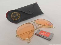 Sunglasses folded beside black Ray-Ban case and tag
