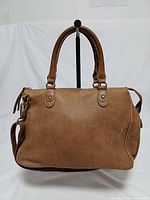 Front view of tan Tribe leather Roots satchel showing overall style, handles and strap.