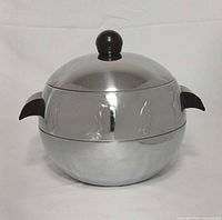 Front view showing spherical chrome server, lid with Bakelite knob, side handle, embossed penguins