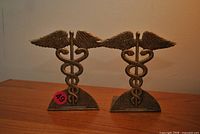 Front view of both brass caduceus bookends on wood surface